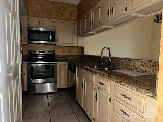 kitchen with stainless steel appliances, dark stone counters, a sink, and dark tile patterned floors