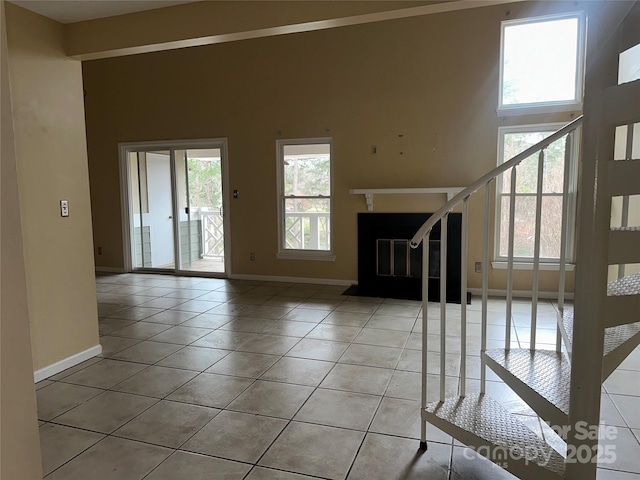 unfurnished living room featuring a towering ceiling, stairs, baseboards, and tile patterned floors