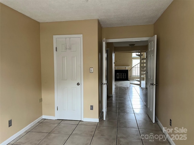 hall with a textured ceiling, baseboards, and tile patterned floors