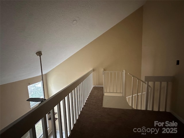 corridor with lofted ceiling, a textured ceiling, and carpet flooring