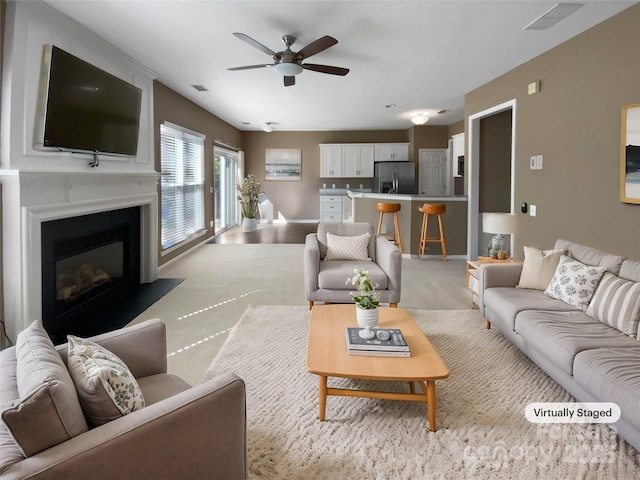 living area with a glass covered fireplace, visible vents, ceiling fan, and baseboards