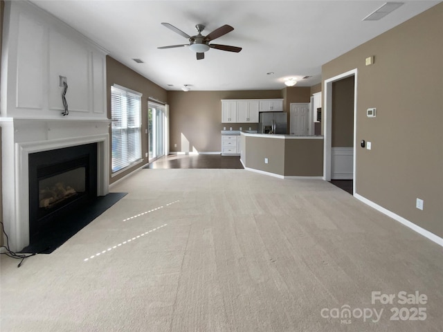 unfurnished living room featuring visible vents, baseboards, ceiling fan, a fireplace with flush hearth, and carpet floors