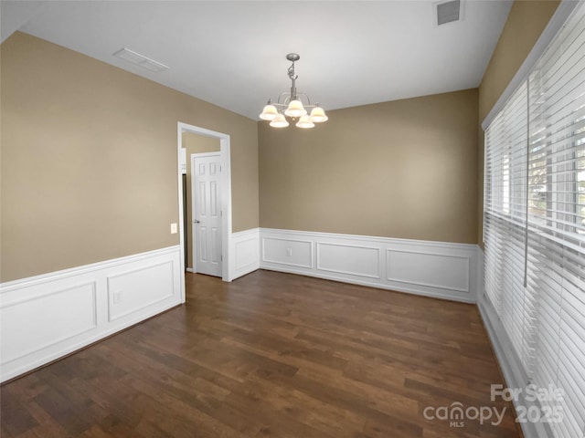 spare room with dark wood-style flooring, visible vents, wainscoting, and an inviting chandelier