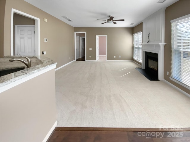 unfurnished living room with light carpet, plenty of natural light, a fireplace, and baseboards