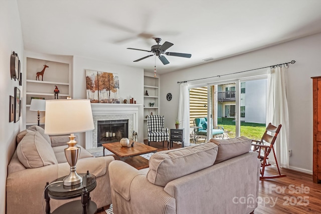 living room with built in shelves, visible vents, a fireplace, and wood finished floors