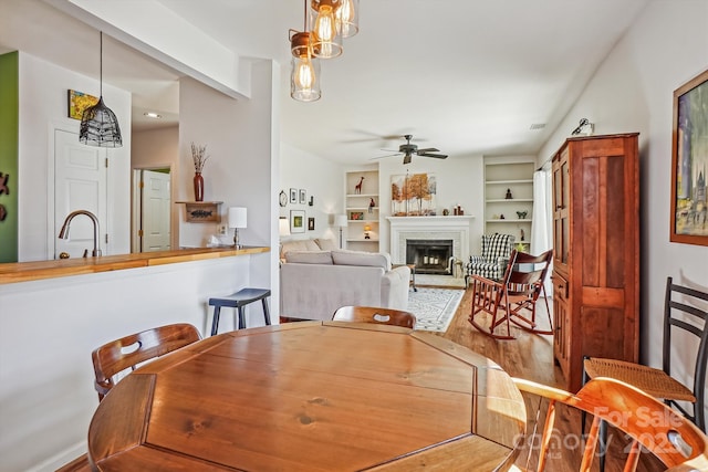 dining area featuring built in shelves, a brick fireplace, ceiling fan, and wood finished floors