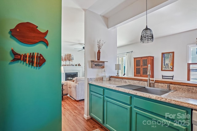 kitchen featuring a sink, light countertops, light wood-type flooring, a fireplace, and green cabinetry