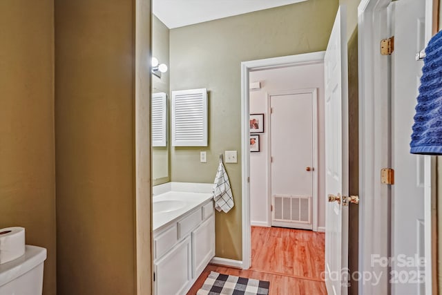 half bathroom featuring toilet, wood finished floors, vanity, visible vents, and baseboards