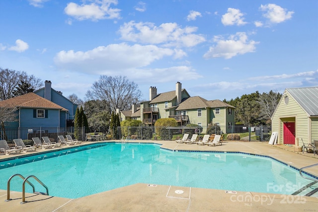 community pool with a patio, fence, and a residential view