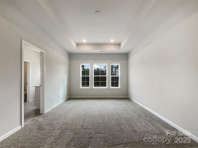 empty room featuring carpet floors, baseboards, and a raised ceiling