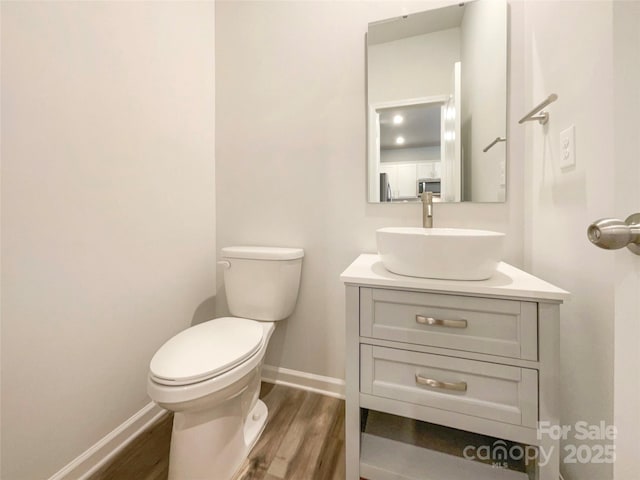 half bathroom with vanity, wood finished floors, toilet, and baseboards