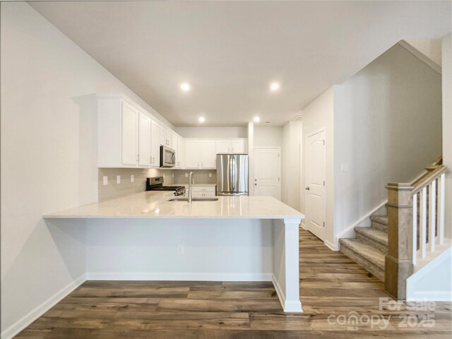 kitchen with stainless steel appliances, light countertops, white cabinets, a sink, and a peninsula