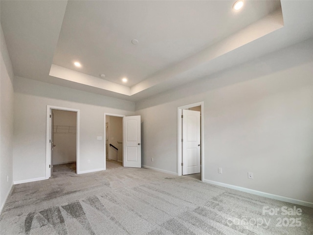 unfurnished bedroom with recessed lighting, a raised ceiling, light colored carpet, and baseboards