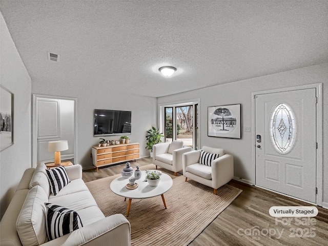 living area with a textured ceiling, wood finished floors, and visible vents