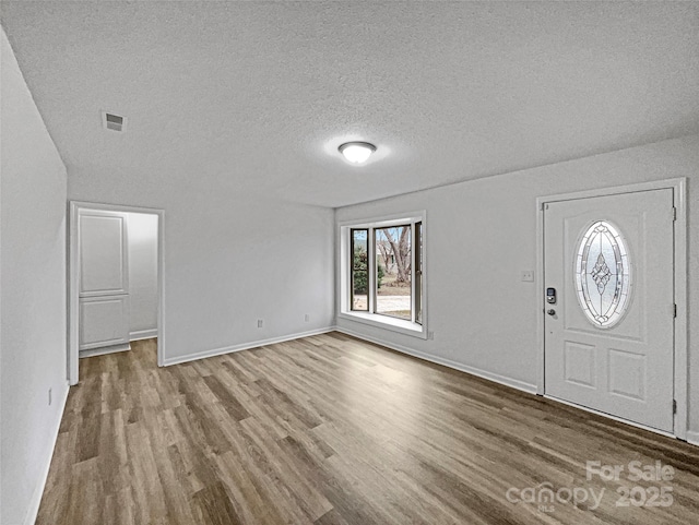 entryway with a textured ceiling, wood finished floors, visible vents, and baseboards