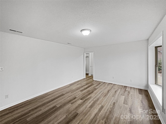 spare room with a textured ceiling, wood finished floors, visible vents, and baseboards