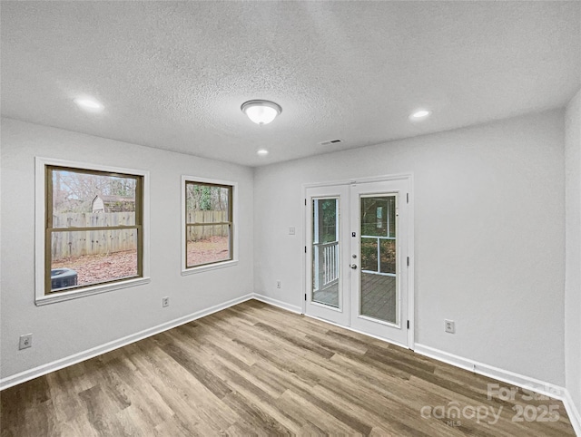 unfurnished room with a textured ceiling, wood finished floors, visible vents, baseboards, and french doors