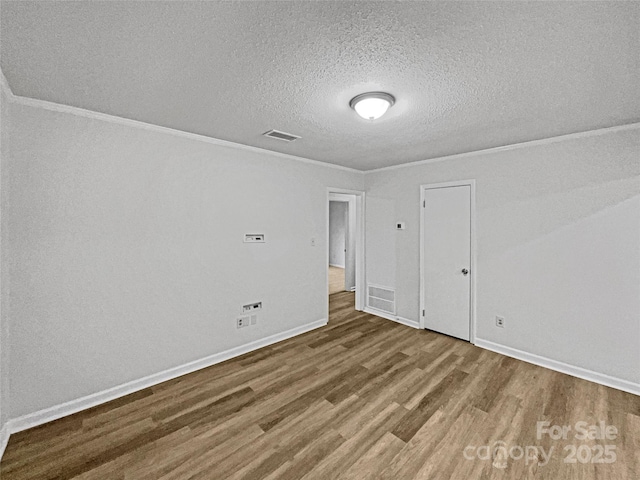 spare room with visible vents, ornamental molding, a textured ceiling, wood finished floors, and baseboards