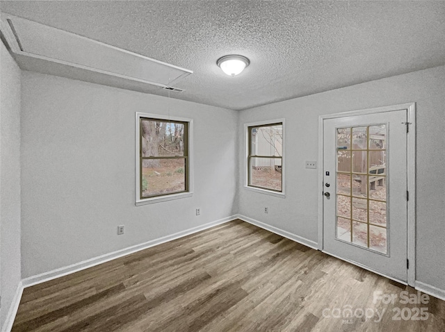 empty room featuring attic access, baseboards, visible vents, wood finished floors, and a textured ceiling