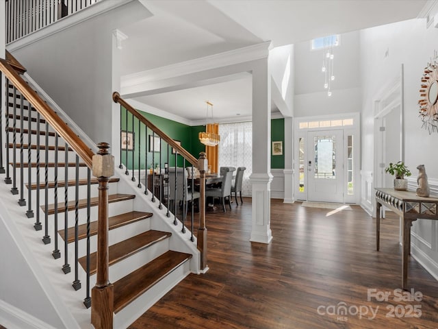 entryway with a wainscoted wall, stairs, wood finished floors, a notable chandelier, and ornate columns