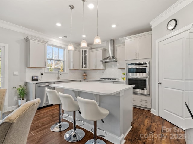 kitchen featuring appliances with stainless steel finishes, light countertops, wall chimney range hood, and ornamental molding