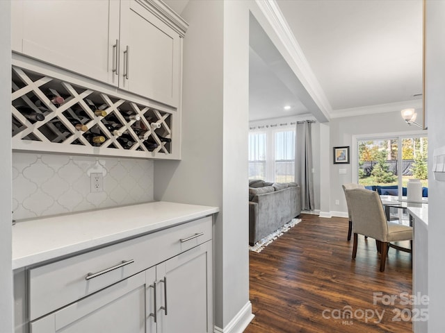 bar with baseboards, dark wood-style flooring, ornamental molding, decorative backsplash, and a bar