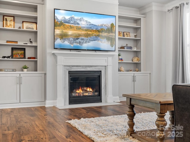 living room with a fireplace, crown molding, built in shelves, and wood finished floors