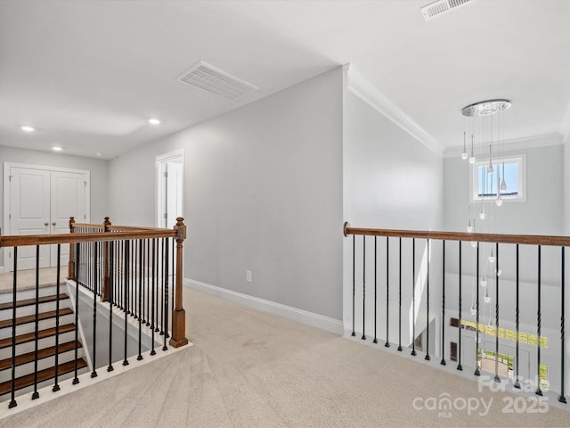 corridor featuring visible vents, baseboards, ornamental molding, an upstairs landing, and carpet flooring