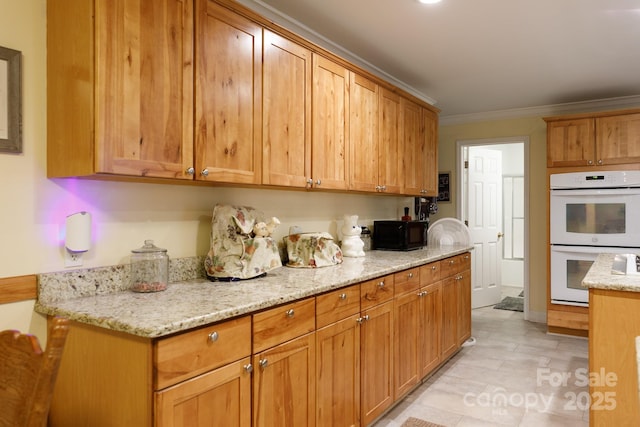 kitchen with black microwave, white double oven, light stone countertops, and crown molding