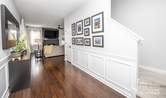 hallway featuring a wainscoted wall, a decorative wall, and dark wood-style flooring