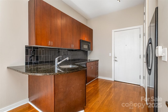 kitchen featuring black appliances, a sink, wood finished floors, dark stone counters, and decorative backsplash