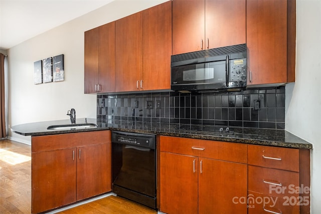 kitchen with dark stone counters, a peninsula, a sink, black appliances, and light wood-style floors