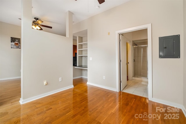 interior space with a spacious closet, electric panel, wood finished floors, and baseboards