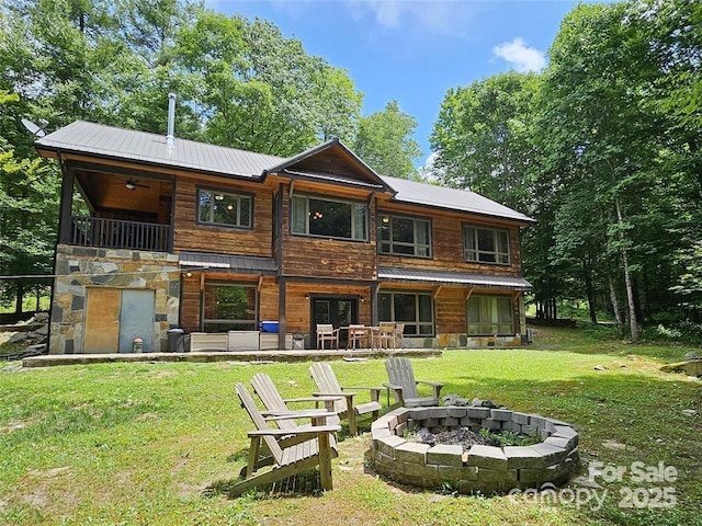 back of house with metal roof, a patio area, a yard, and a fire pit