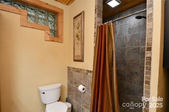 full bath featuring a tile shower, toilet, and tile walls