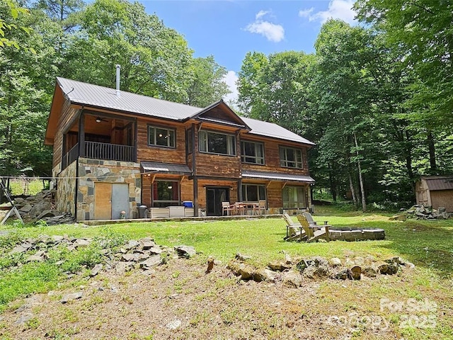 rear view of property with stone siding, a fire pit, metal roof, and a lawn