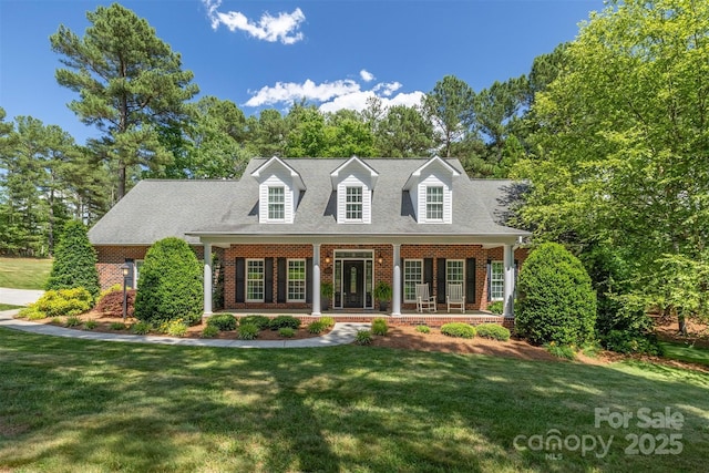 new england style home featuring covered porch, brick siding, and a front lawn