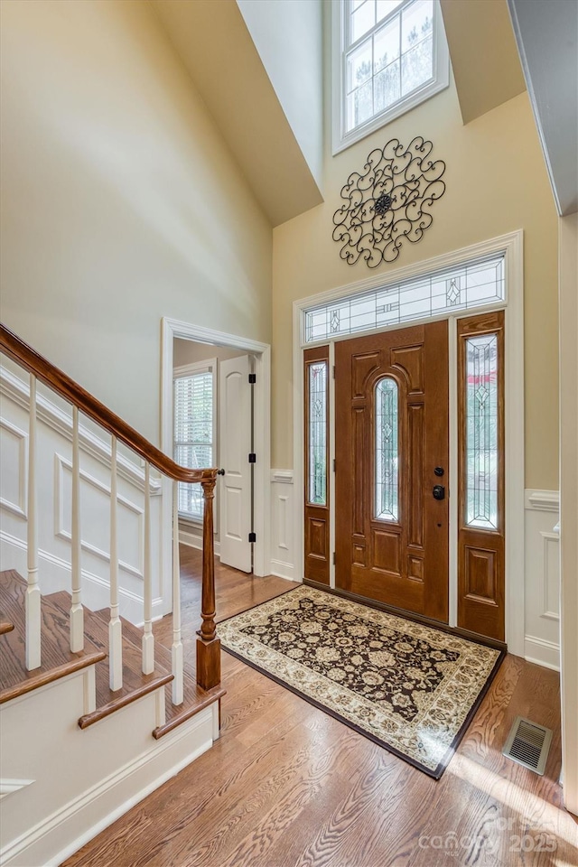 foyer entrance featuring wainscoting, visible vents, a towering ceiling, and wood finished floors