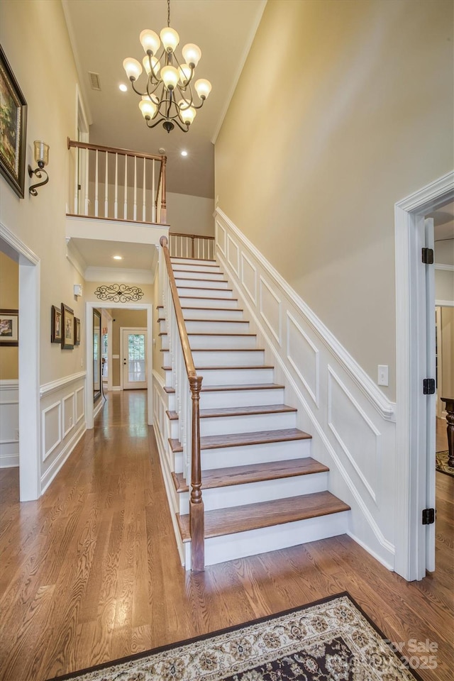 stairway featuring a chandelier, a decorative wall, a high ceiling, wood finished floors, and ornamental molding