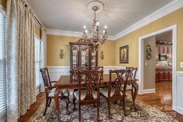 dining room featuring dark wood-style floors, ornamental molding, a notable chandelier, and wainscoting