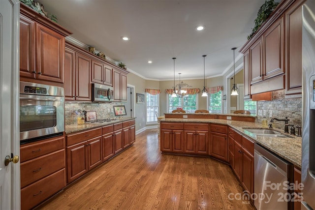 kitchen with crown molding, stainless steel appliances, light wood-style floors, a sink, and a peninsula