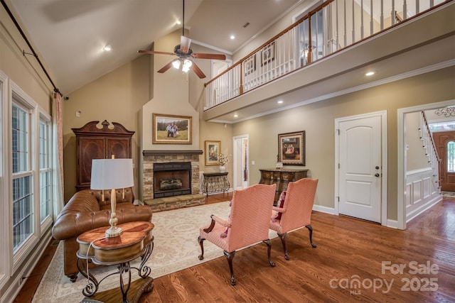 living area featuring a ceiling fan, high vaulted ceiling, wood finished floors, and a stone fireplace