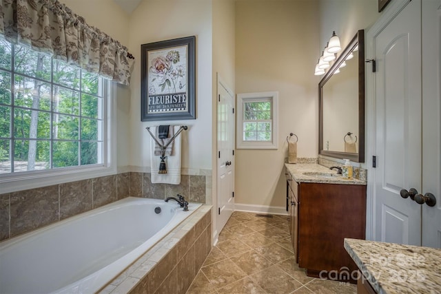 bathroom featuring tile patterned flooring, vanity, baseboards, and a bath