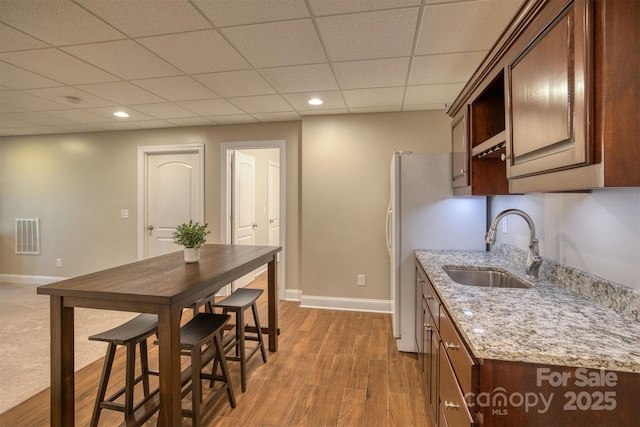 kitchen with baseboards, wood finished floors, light stone countertops, a paneled ceiling, and a sink