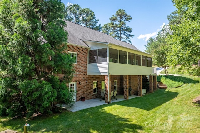 back of house with a shingled roof, a patio, a sunroom, a yard, and brick siding