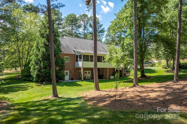 back of house featuring a sunroom, a patio area, a lawn, and brick siding