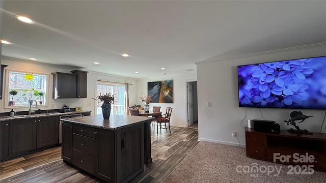 kitchen with dark countertops, crown molding, a sink, and a center island