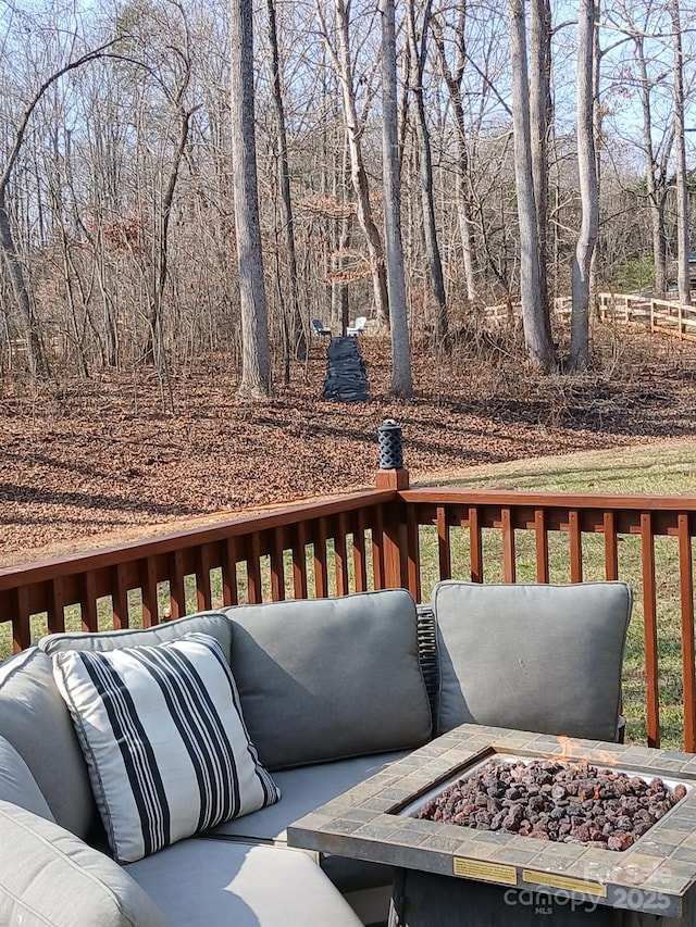 wooden terrace with an outdoor living space with a fire pit and a view of trees