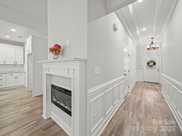 hall featuring a decorative wall, light wood-type flooring, a wainscoted wall, and ornamental molding