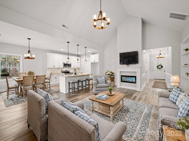 living room featuring a glass covered fireplace, a notable chandelier, visible vents, and light wood finished floors